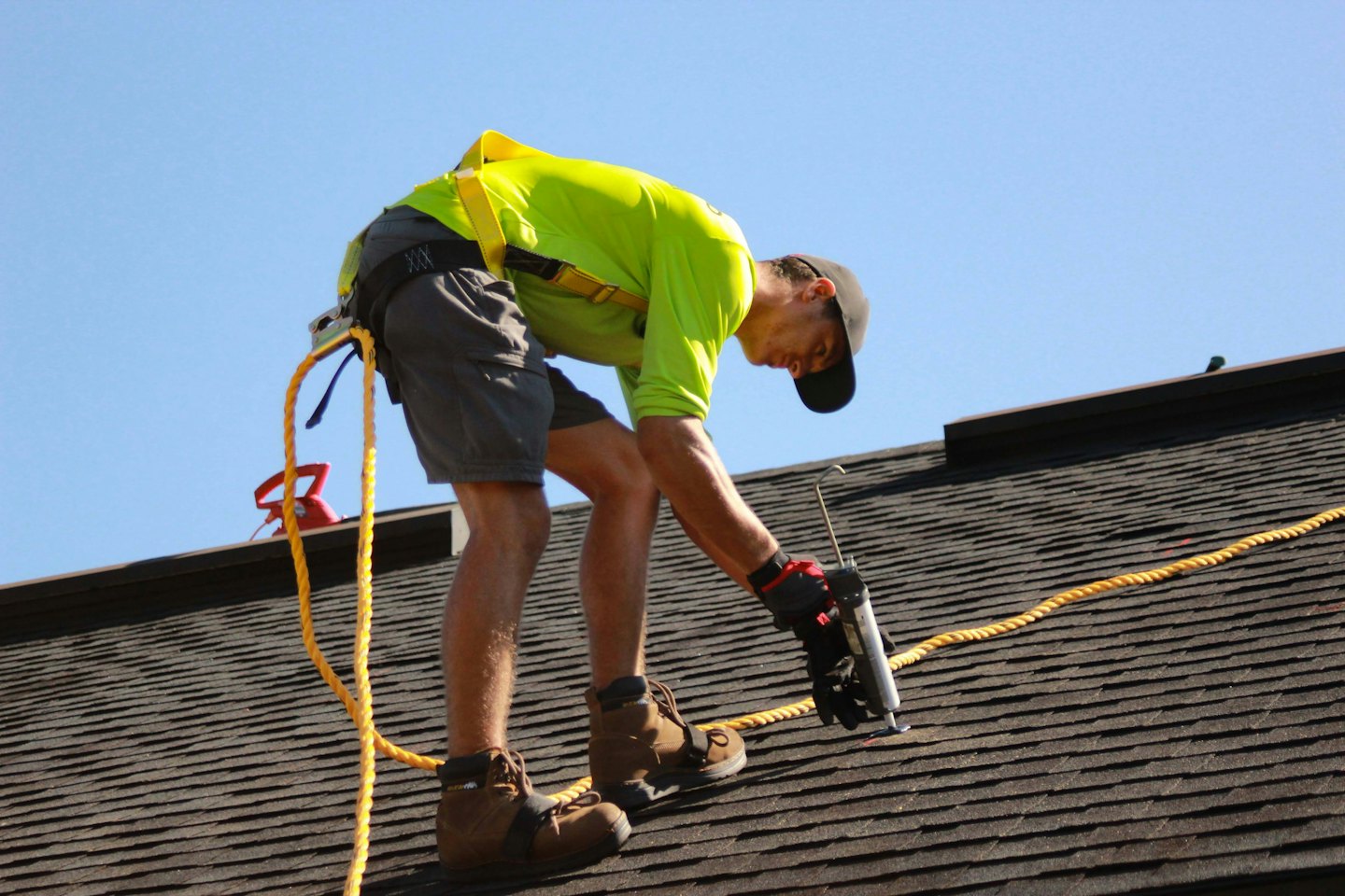 Roofer applying sealant to asphalt shingles under blue sky.
