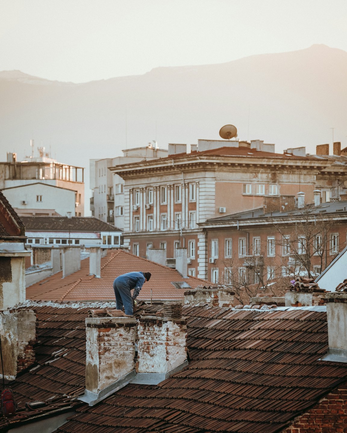 Construction worker repairs old terracotta roof in historic city.