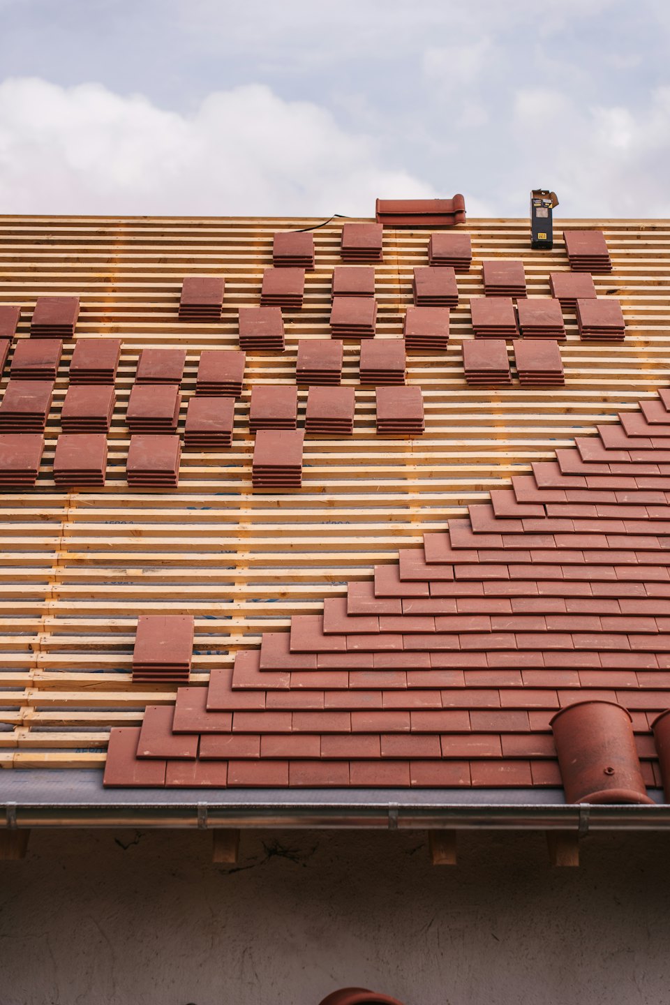 Workers installing reddish-brown clay tiles on a residential roof.