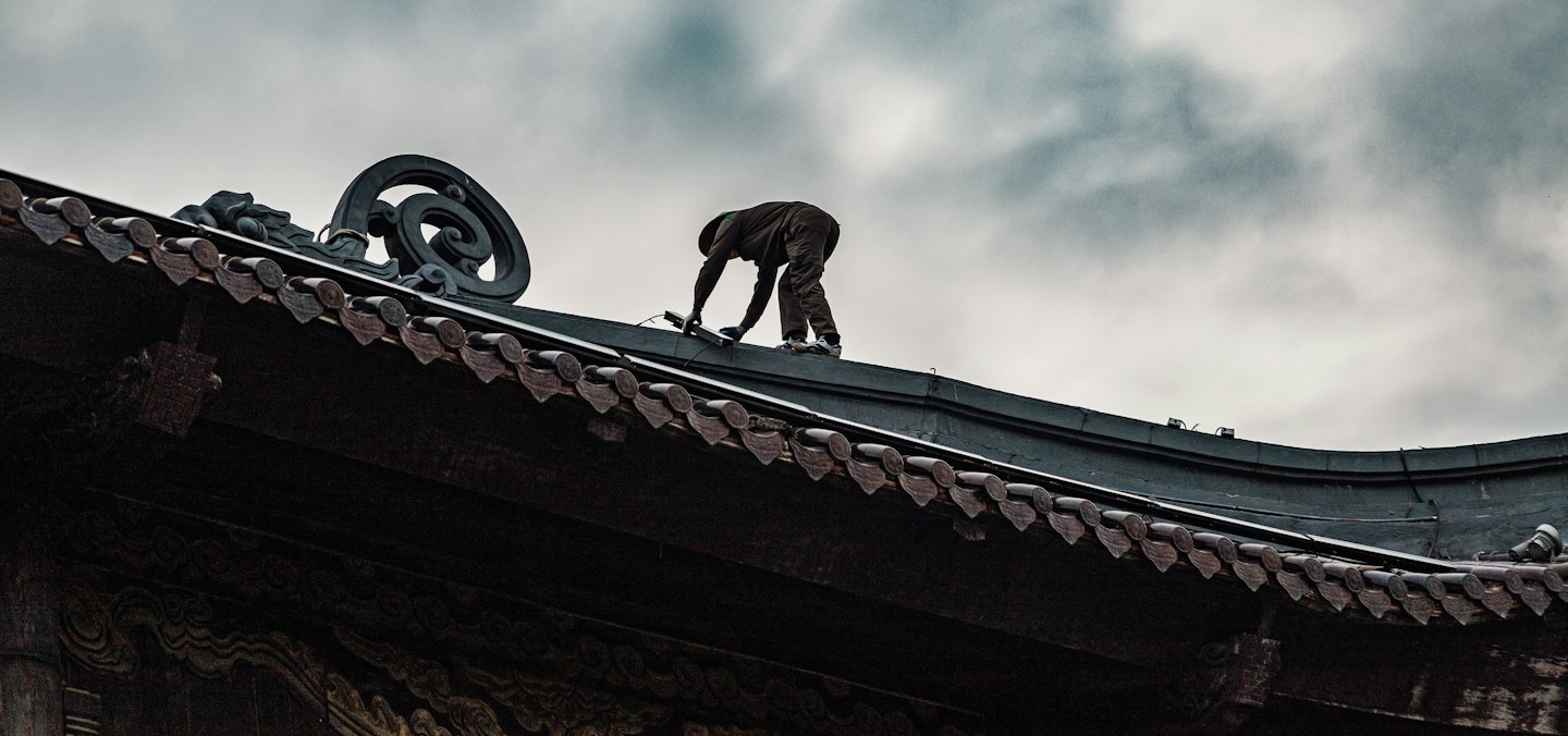 Worker fixing equipment on an old tiled roof.
