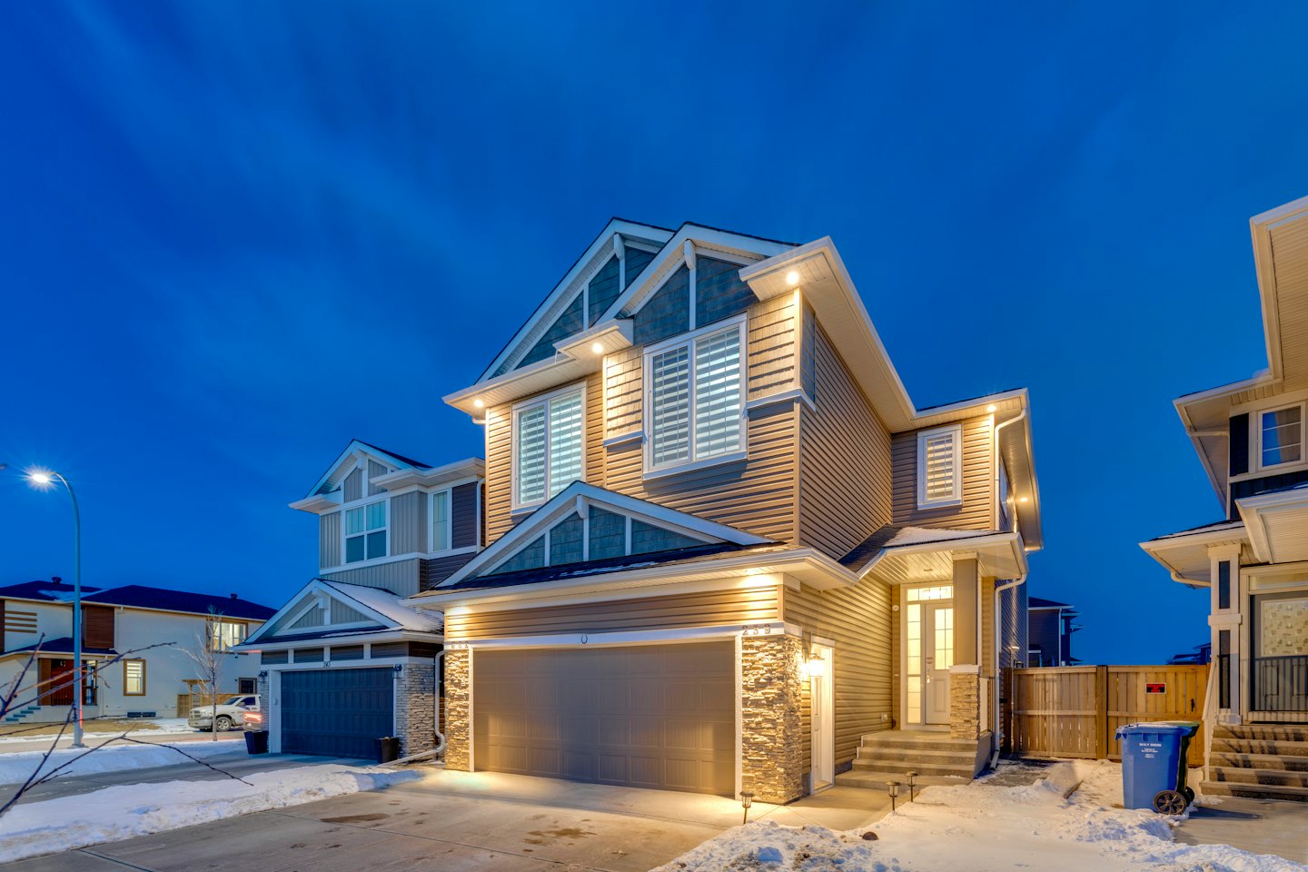 Modern suburban house with snow covered yard at dusk.